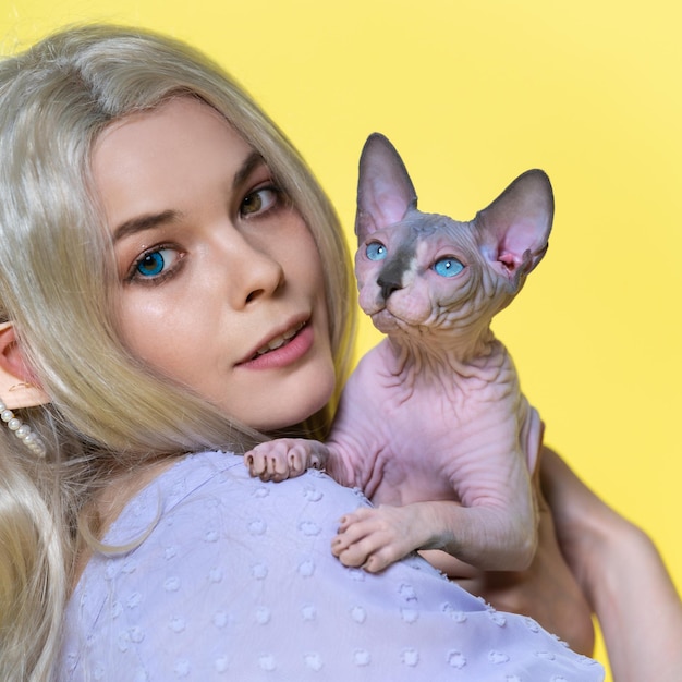 Portrait of young female cosplay elf holding sphinx kitten in hands smiling and looking at camera