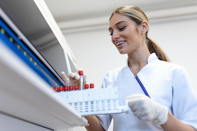 Portrait of a young female laboratory assistant making analysis with test tubes and analyzer machines sitting at the modern laboratory