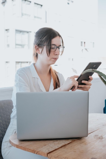 Portrait young female programmer focus on jobworking simultaneously with laptop and tabletCorrecting errors and mistakessolving frequent questions and teaching new methodsTerraceworking from home