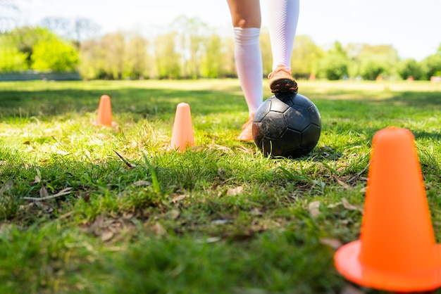 Portrait of young female soccer player running around cones while practicing with ball on field. Sports concept.