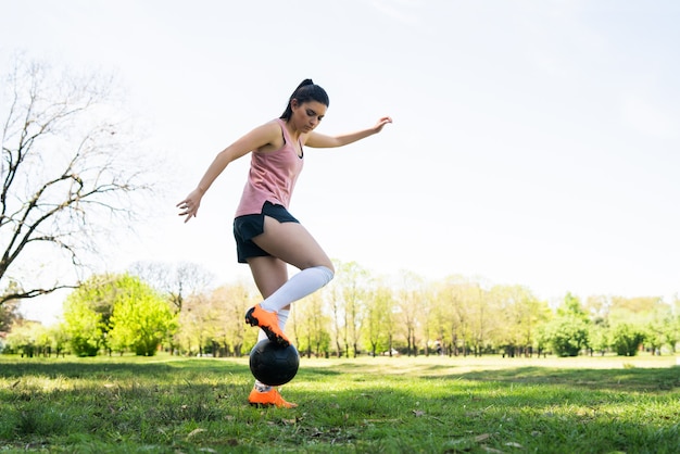 Portrait of young female soccer player running around cones while practicing with ball on field. Sports concept.