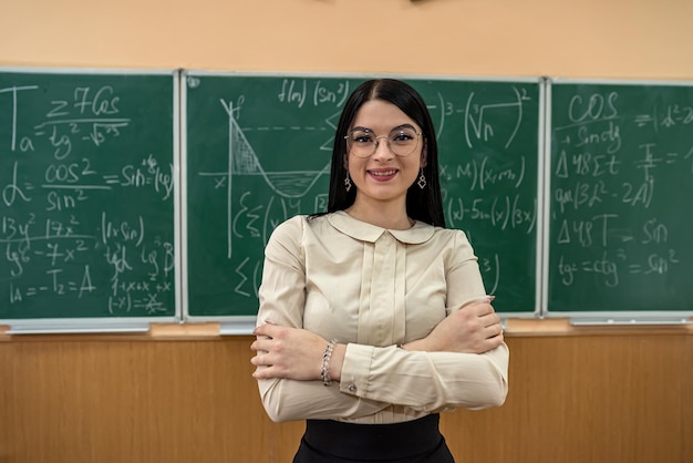 Portrait of young female teacher against blackboard with math formula in classroom