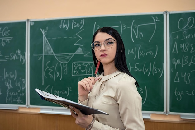 Portrait of young female teacher against blackboard with math formula in classroom