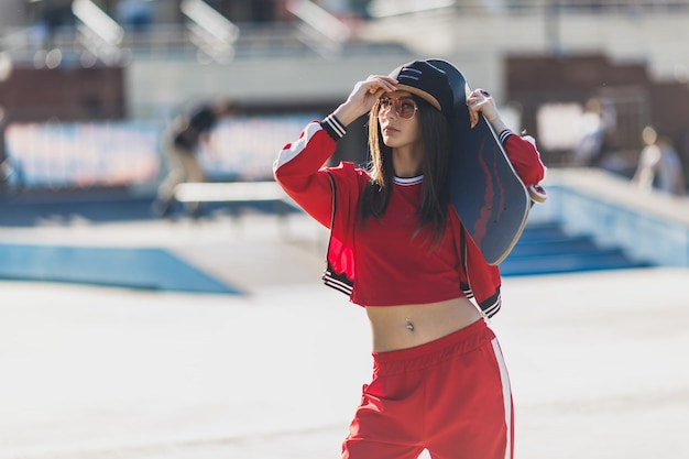 Portrait of young female wearing black hat red clothing skateboarder holding her skateboard