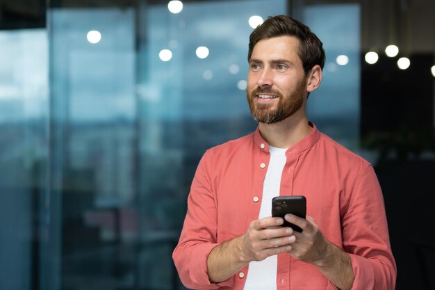 Portrait of a young freelancer man manager standing in the office and using a mobile phone he looks