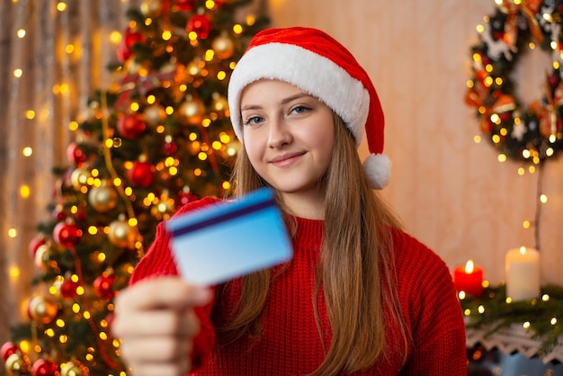 Portrait of a young girl in Christmas hat holding plastic credit card Payments purchases with a help of credit card during Christmas holidays