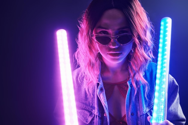 Portrait of young girl in glasses holding light sticks in red and blue neon in studio