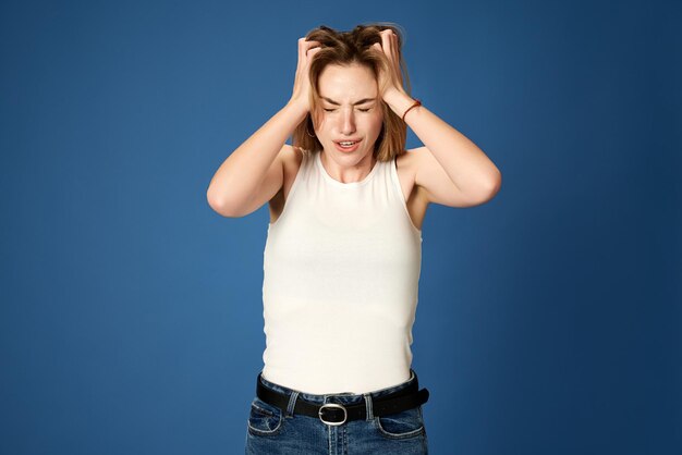 Portrait of young girl holding head with hands suffering from stress and depression against blue