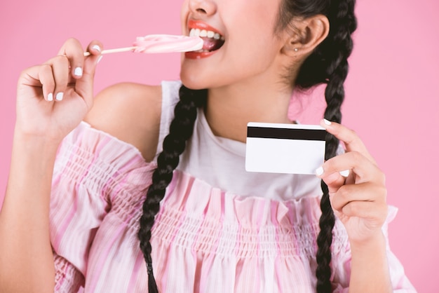 Portrait of young girl showing credit card  with candy over pink background,Easy Business concept.