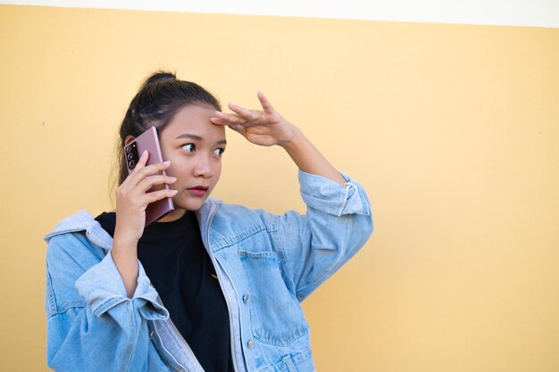 Portrait young girl wear jacket jean and use mobile on brown background.