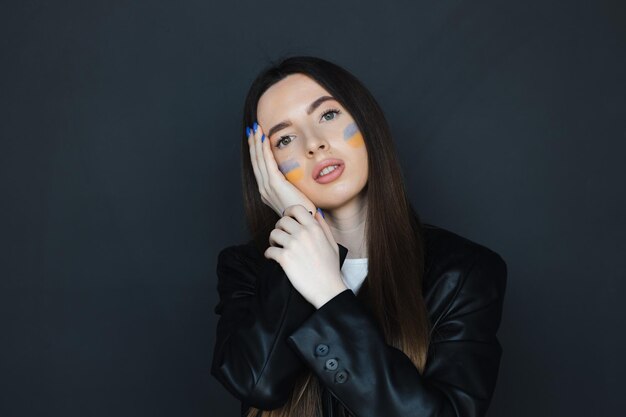 Portrait of young girl with blue and yellow ukrainian flag on her cheek on black background