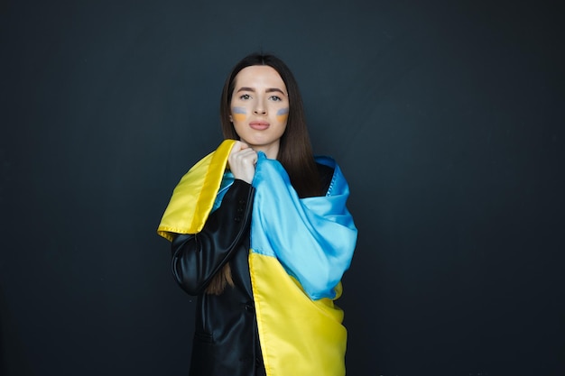 Portrait of young girl with blue and yellow ukrainian flag on her cheek on black background