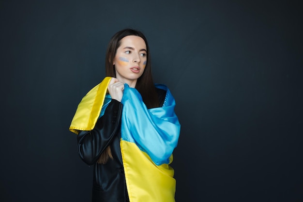 Portrait of young girl with blue and yellow ukrainian flag on her cheek on black background