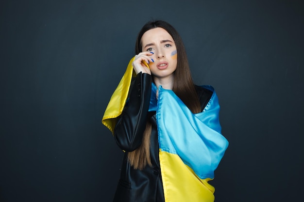 Portrait of young girl with blue and yellow ukrainian flag on her cheek on black background