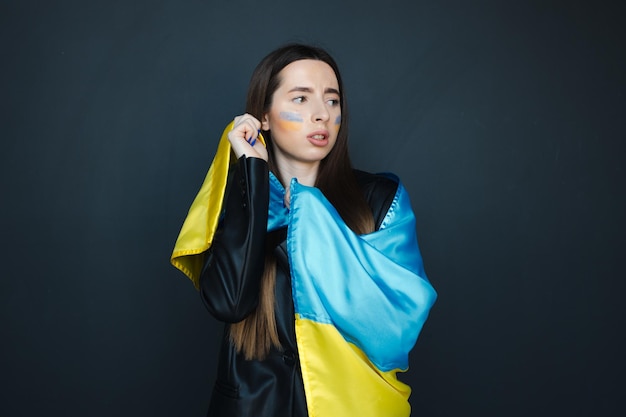 Portrait of young girl with blue and yellow ukrainian flag on her cheek on black background