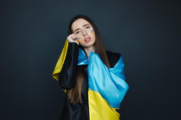 Portrait of young girl with blue and yellow ukrainian flag on her cheek on black background