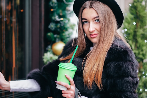 Portrait of young girl with a cup of coffee walking on the street