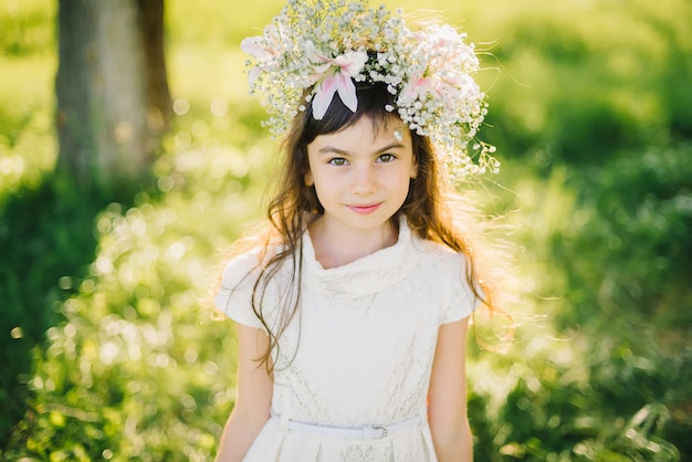 Portrait of a young girl with a wreath of flowers on her head on a meadow