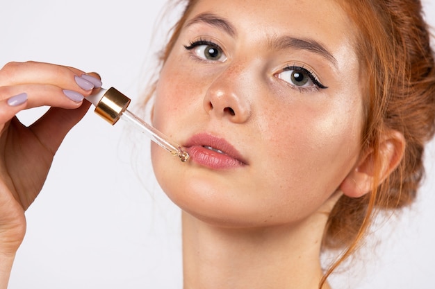 Portrait of a young girl without makeup applies a serum to her face with a pipette. Cosmetology, skin care, spa, natural cosmetics. Enlarged photo on white wall. High quality photo