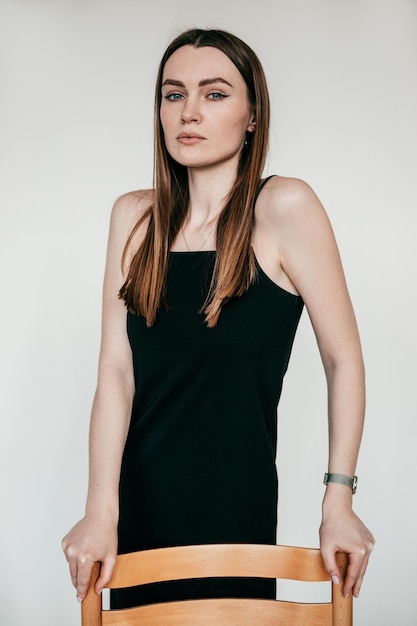 Portrait of young gorgeous serious woman with long dark hair wearing black dress standing leaning on