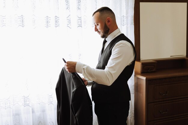 Portrait of a young groom with a beard at home before the wedding ceremony Handsome man with a black beard wearing a classic suit Male portrait