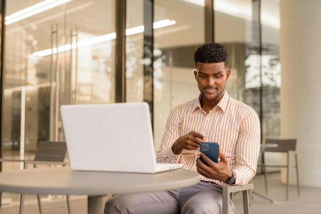 Portrait of young handsome African businessman using laptop computer at coffee shop