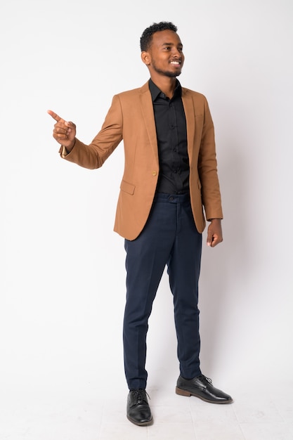 Portrait of young handsome African businessman wearing brown suit against white wall