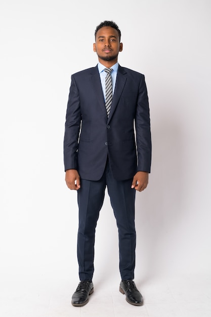 Portrait of young handsome African businessman wearing suit against white wall