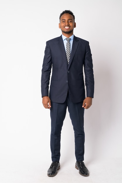 Portrait of young handsome African businessman wearing suit against white wall