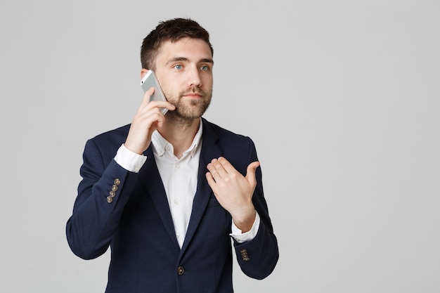 Portrait young handsome angry business man in suit talking on phone looking at camera.