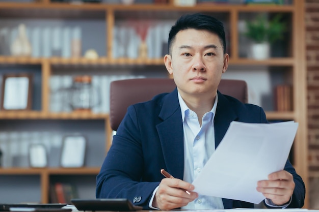 Portrait of young handsome asian businessman director working with documents in office serious looking at camera