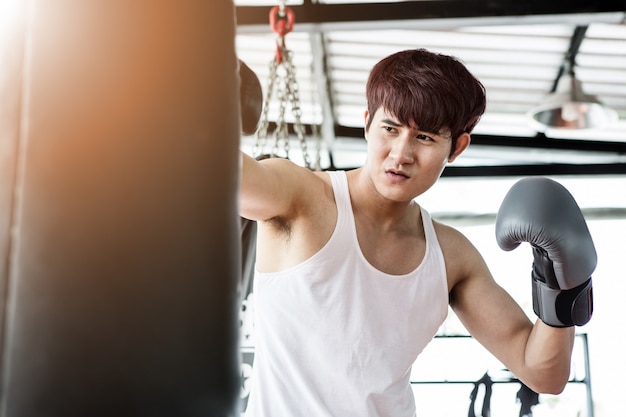 Portrait of a young handsome asian man practicing boxing on a punching bag at the sport club