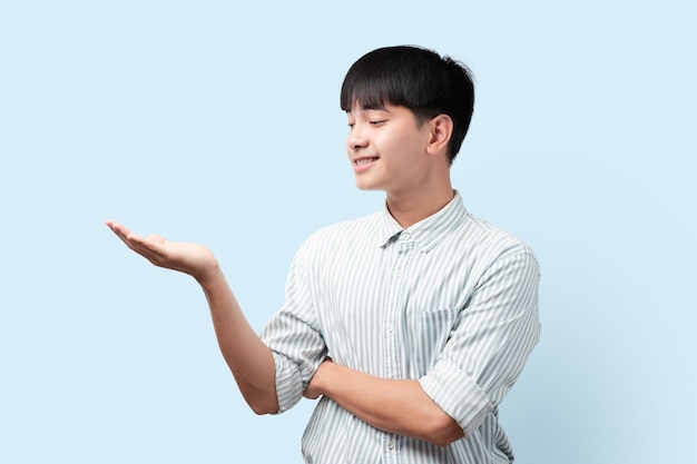 Portrait of young handsome Asian man shows holding out hand with palm Asian man standing on blue