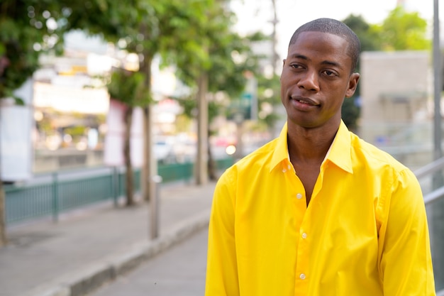 Portrait of young handsome bald African businessman exploring the city streets of Bangkok