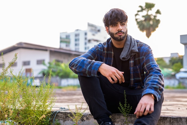 Portrait of young handsome bearded Indian hipster man in the city streets outdoors