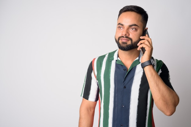 Portrait of young handsome bearded Indian man against white wall