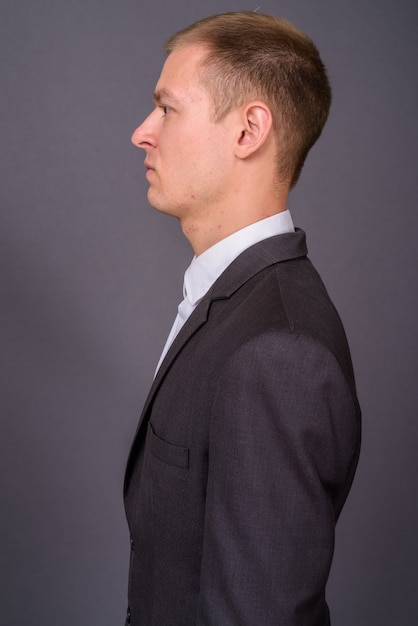 Portrait of young handsome businessman against gray wall