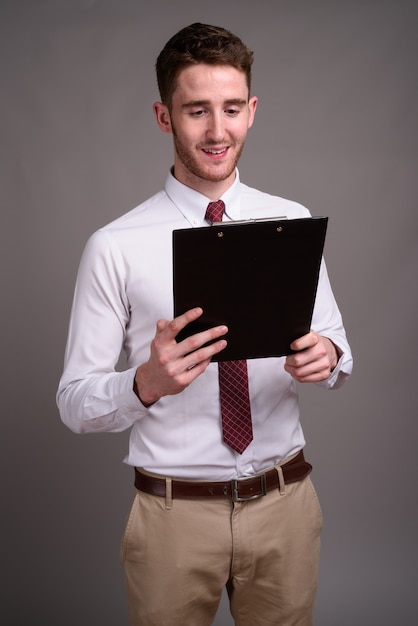 Portrait of young handsome businessman against gray