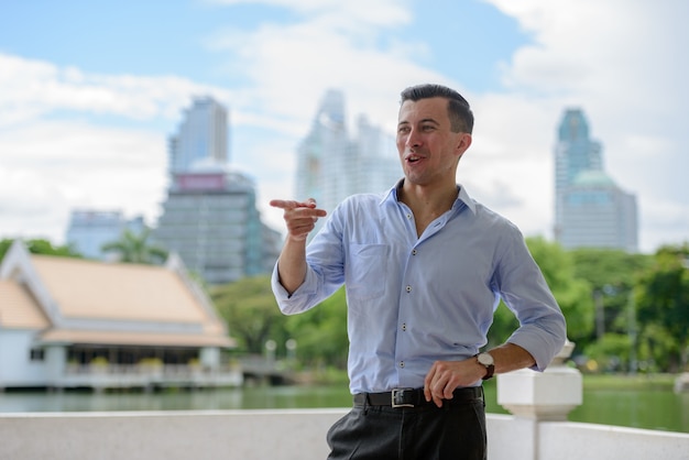 Portrait of young handsome businessman against view of the lake at the park