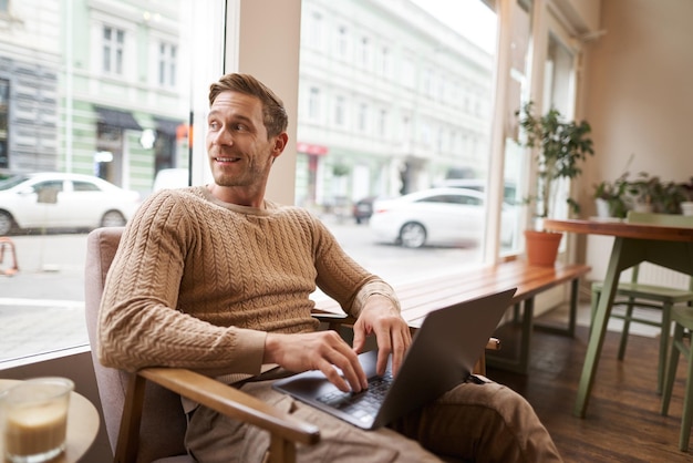 Photo portrait of young handsome businessman a man with laptop sitting in coffee shop on chair and working