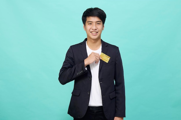 Portrait Young handsome businessman in a suit holding yellow credit card isolated in a blue studio