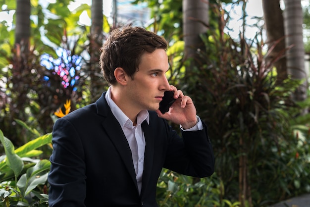 Portrait of young handsome businessman talking on the phone at the park