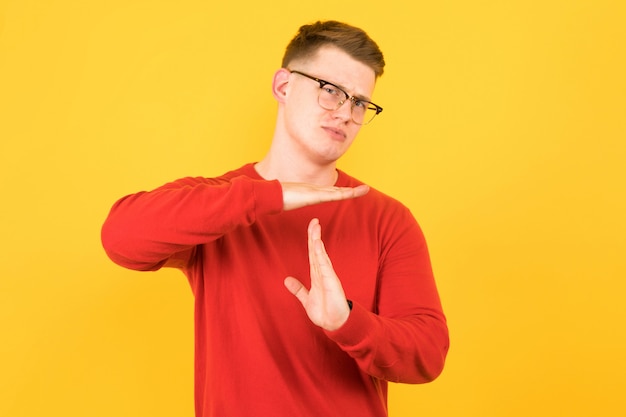 Portrait of young handsome disappointed guy in red sweater showing time-out gesture