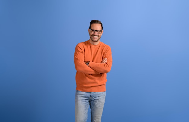 Photo portrait of young handsome entrepreneur with arms crossed smiling and posing on blue background