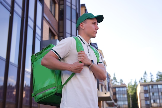 Portrait of young handsome happy courier guy smile food delivery man with green thermo box for food