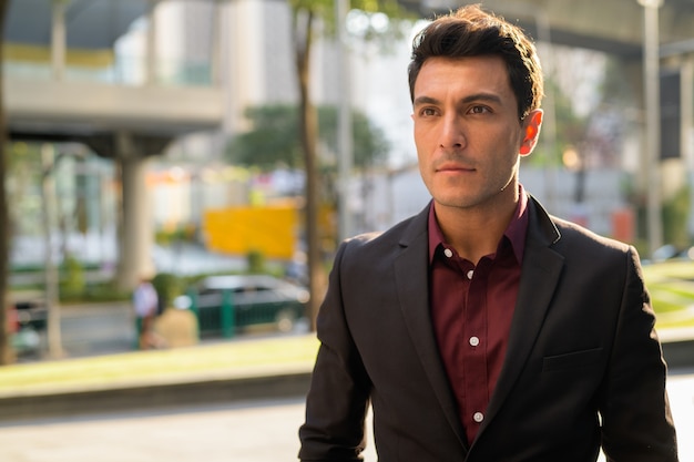 Portrait of young handsome Hispanic businessman in the city streets outdoors