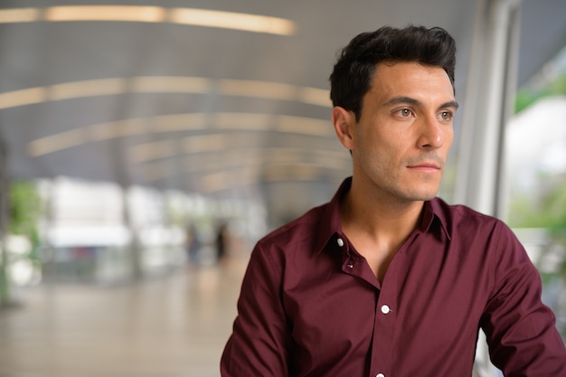 Portrait of young handsome Hispanic businessman on footbridge at the city