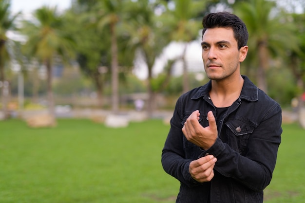 Portrait of young handsome Hispanic man in the park outdoors