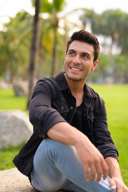 Portrait of young handsome Hispanic man in the park outdoors