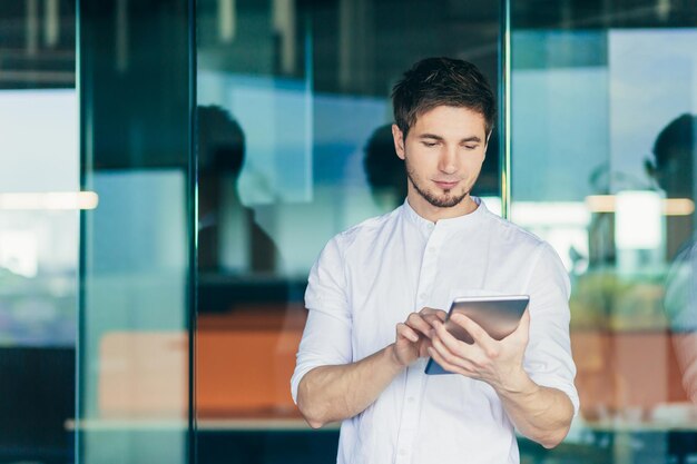 Portrait of a young handsome male businessman freelancer Standing in the office holding a tablet in his hands working typing